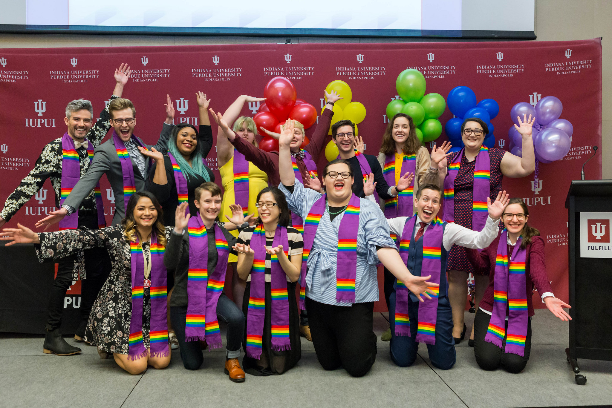 14 students smiling while wearing colorful clothing with balloons