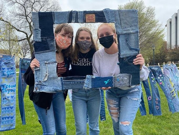 three students wearing masks and holding up a picture frame made up of denim