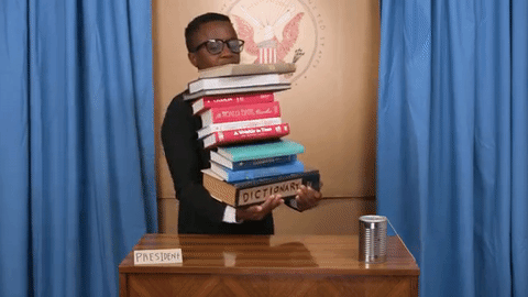 gif of a boy carrying too many books and dropping them
