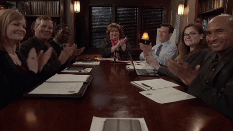 gif of a team of coworkers sitting around a table and clapping