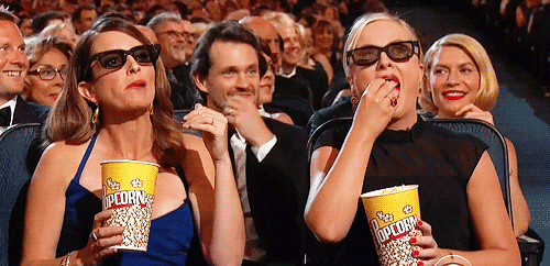 gif of Amy Poehler and Tina Fey snacking on popcorn, appearing to be watching a movie off-screen